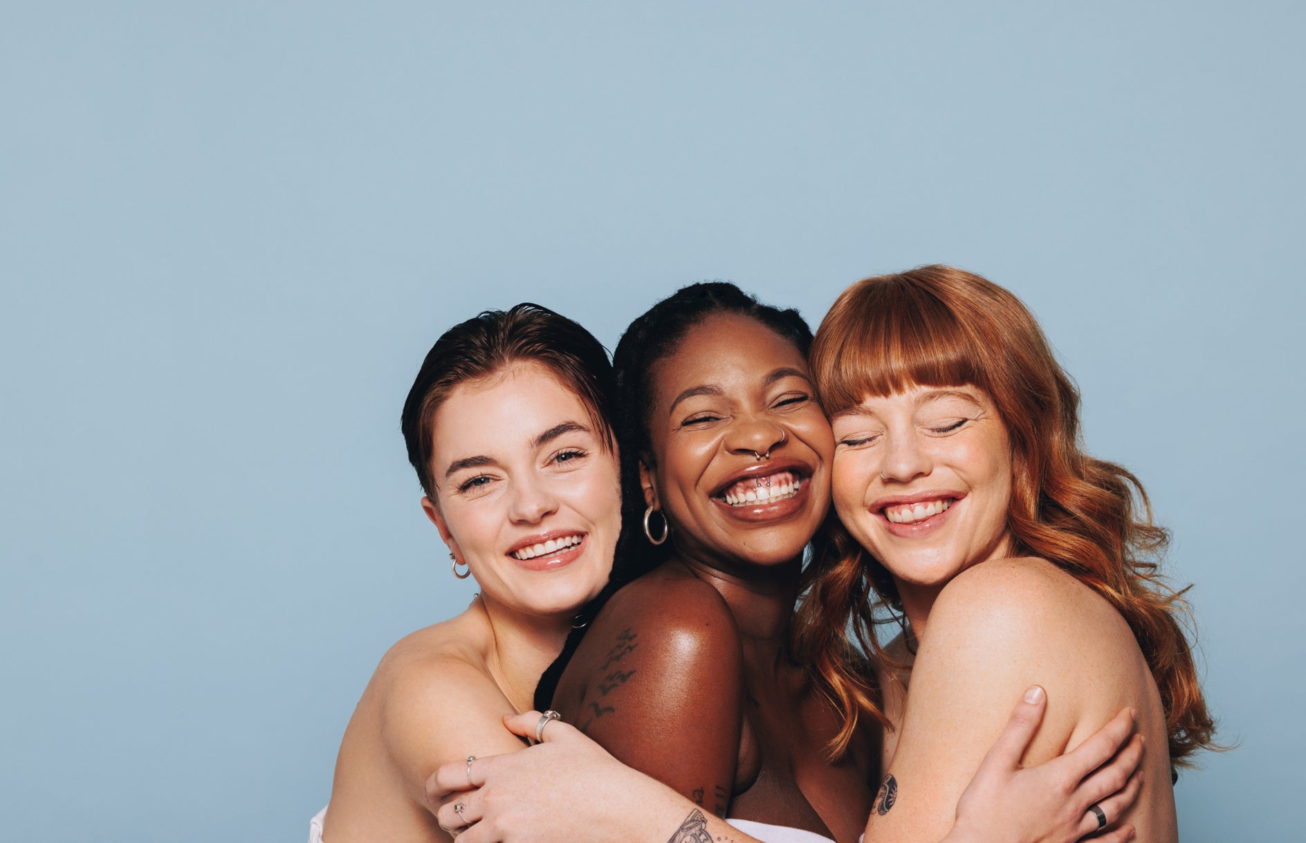 Three women hugging and smiling against a light blue background