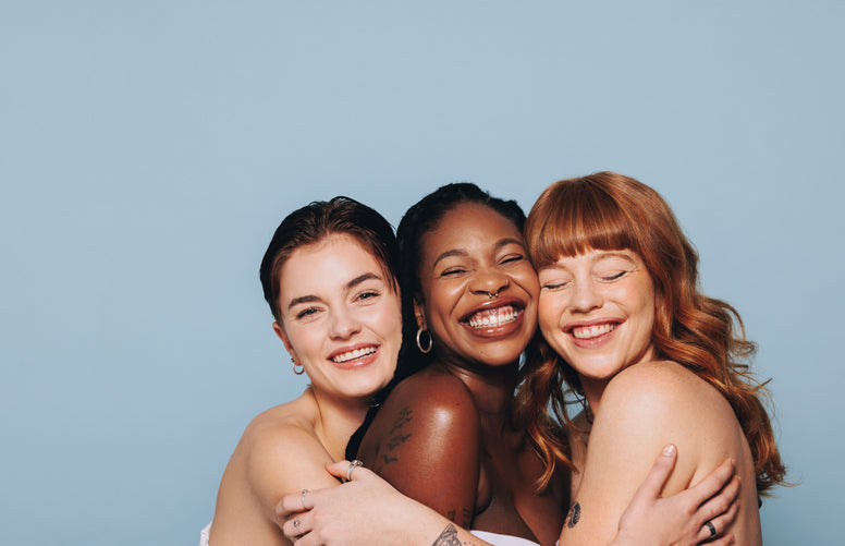 Three women hugging and smiling against a light blue background